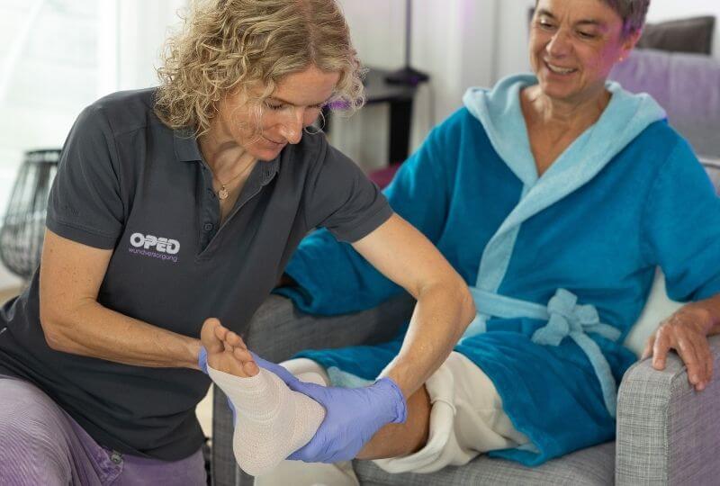 Wundexpertin der OPED Wundversorgung legt einer älteren Patientin im häuslichen Umfeld fachgerecht einen Kompressionsverband an.