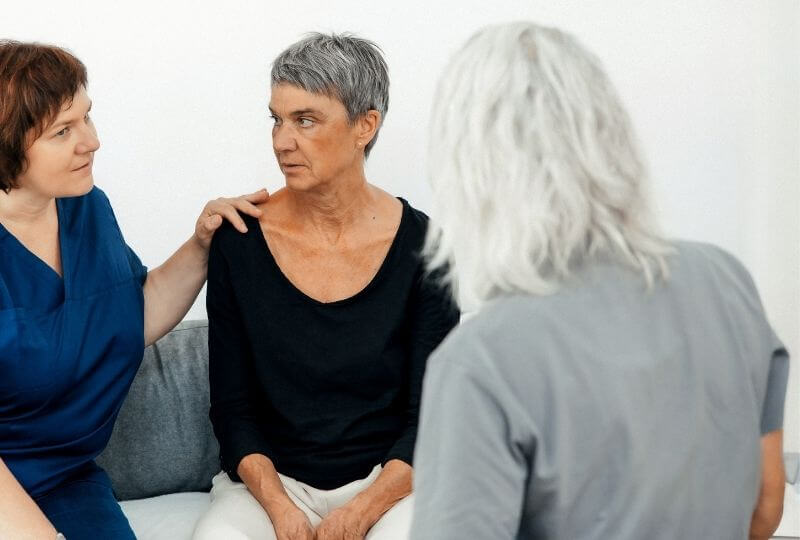 Drei Personen im Gespräch sitzend auf einer Couch im häuslichen Umfeld.