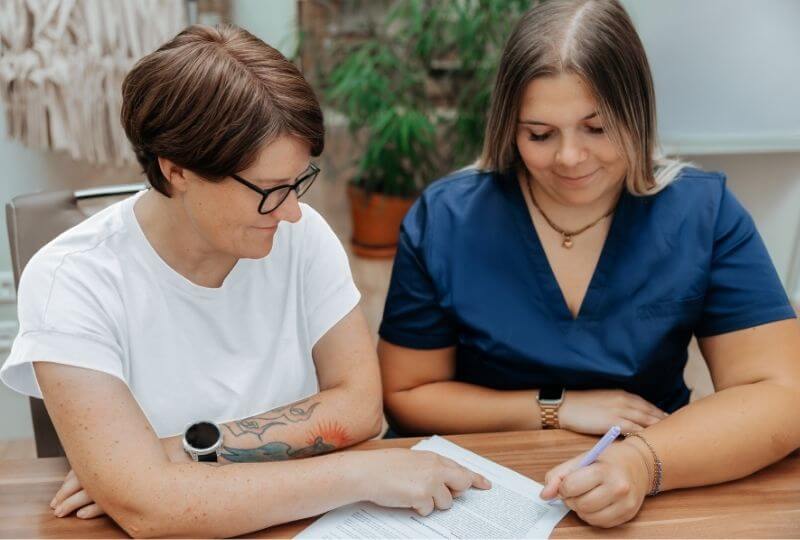 Zwei Frauen sitzen an einem Schreibtisch. Mitarbeiterin eines Pflegedienstes unterschreibt Kooperationsvereinbarung bei der OPED Wundversorgung