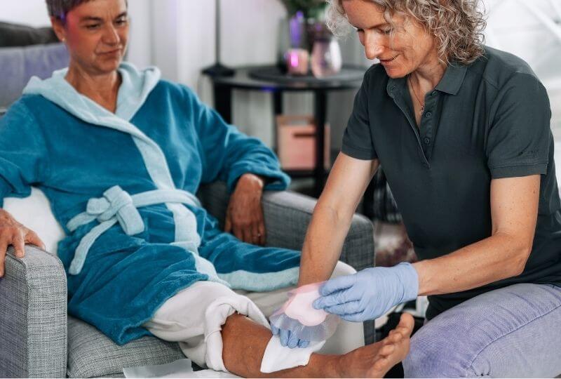 selbstständige Wundversorgerin versorgt Wunde am Bein einer Patientin im heimischen Umfeld